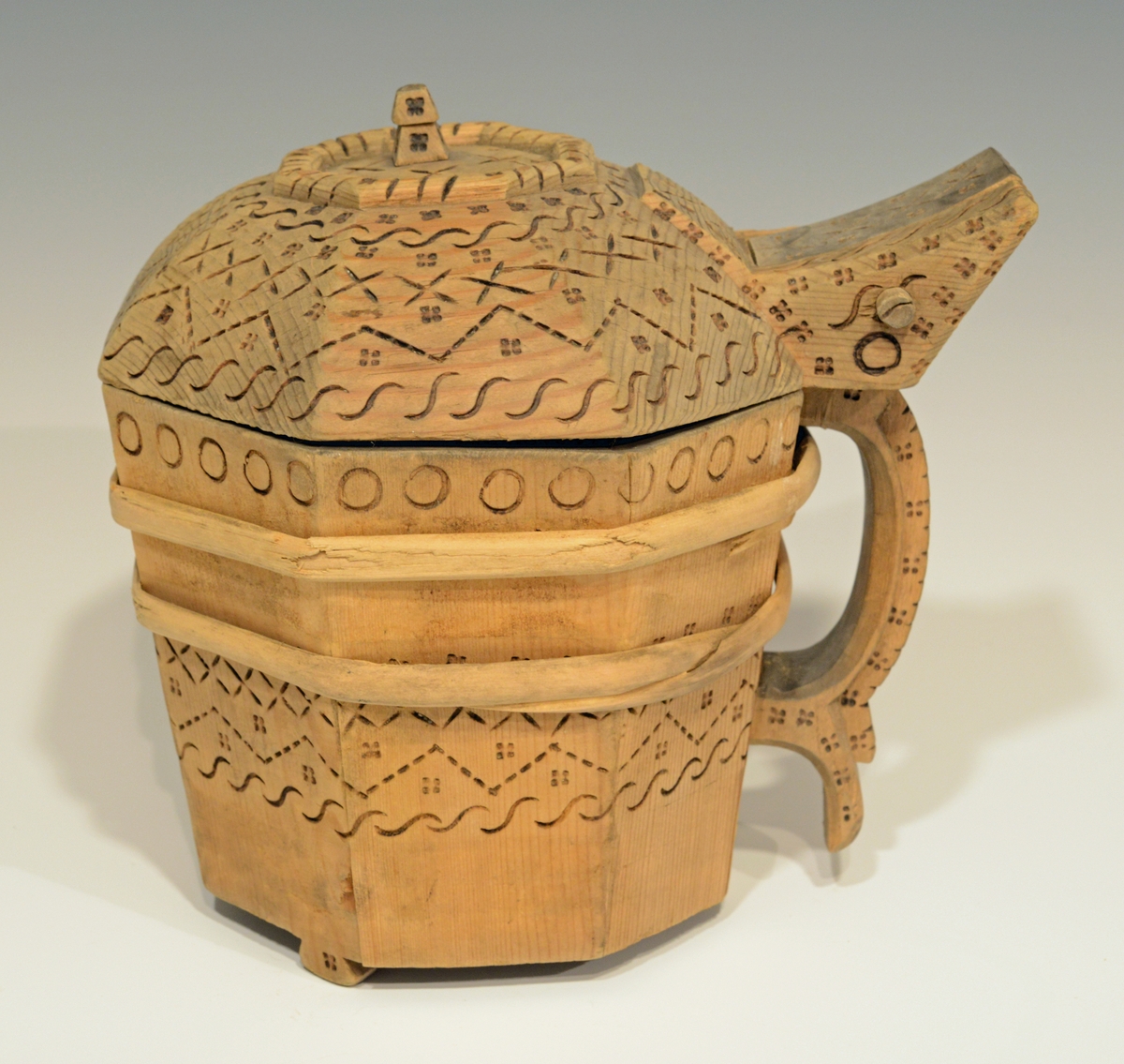 Fra katalog: Ottekantet smørkande og stav med hank og laak og tre smaa føtter, utvendig svimerket og en slynget ring oppe paa laaket, indvendig
rik rosette. Under staar brændemerket: A OSS 1823,