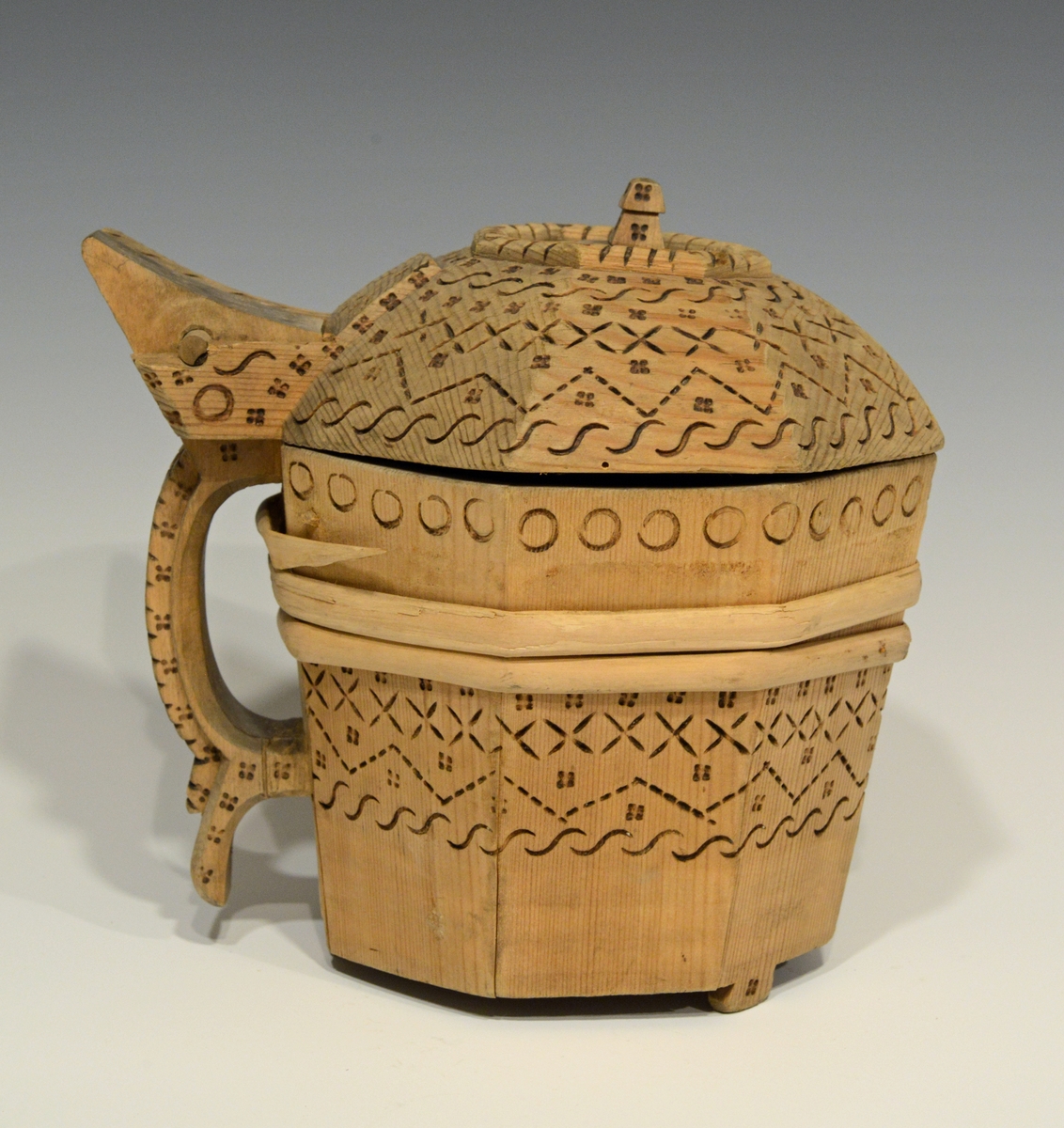 Fra katalog: Ottekantet smørkande og stav med hank og laak og tre smaa føtter, utvendig svimerket og en slynget ring oppe paa laaket, indvendig
rik rosette. Under staar brændemerket: A OSS 1823,