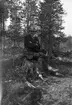 Man sittande på en stubbe i skogen.