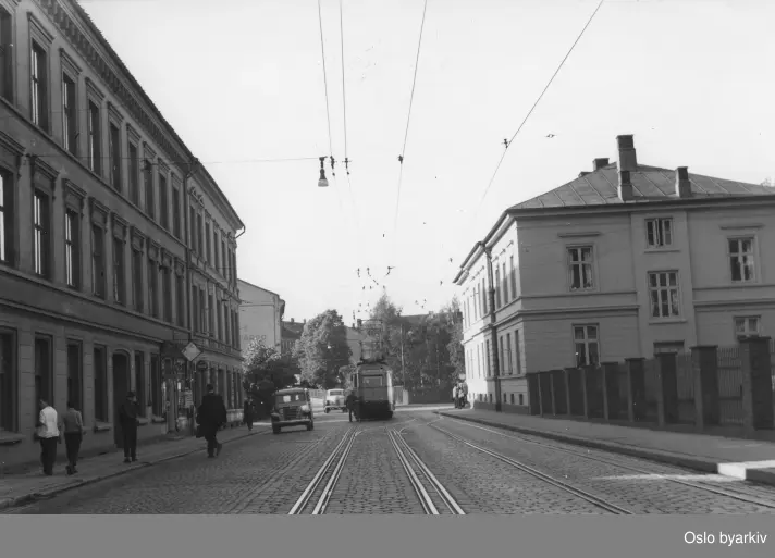 "Oslo gate ved Oslo Hospital og Gamlebyen kirke. Ekebergtrikk på vei til Ljabru. Den doble skinnegangen er en smart løsning på et sporgeomterisk og trafikalt problem. Ekebergbanens vogner kunne tillate seg å ha større hastighet når de skulle passere sporvekselen i innkjøringa til vendesløyfa i Gamlebyen og like etter måtte forsere en ganske lang dødseseksjon på kjøreledningen som skilte mellom bytrikkens 600 volt og Ekebergbanens 1200 volt kjørespenning. Etter reglementet skulle en motveksel passeres med sakte fart, men ved hjelp av dobbeltsporet kunne man tillate trikken som skulle pasere dødseksjonen å ha større hastighet og dermed lettere ha fart nok til å forsere dødseksjonen og ""rekke over""."