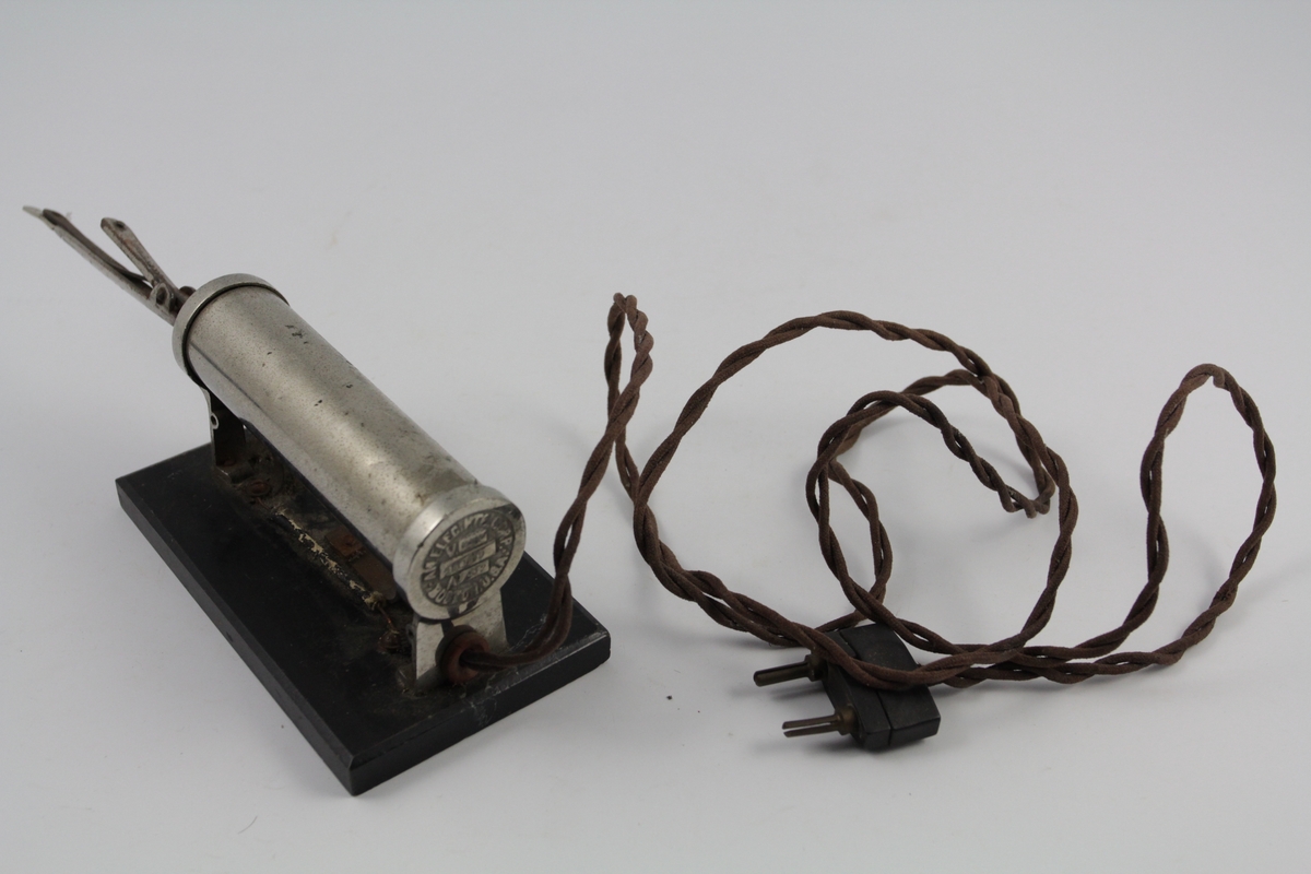 a) Krølltang består av to deler. Underdel som har vulstform, overdel rørformet og spent fast m/fjær til underdel. 
b) Varmeelement på sokkel m/elektrisk kobling.