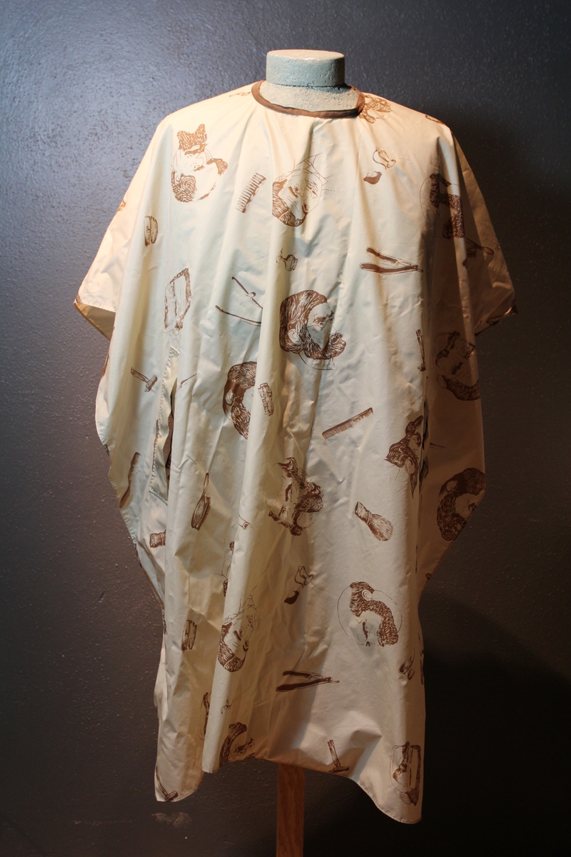 Form: avrundet, rektangulært stykke med halsringning, lukking bak. Stoffet har dekor som viser tegninger av barbersaker, børster og historiske menn med frisert hår, skjegg og/eller bart.