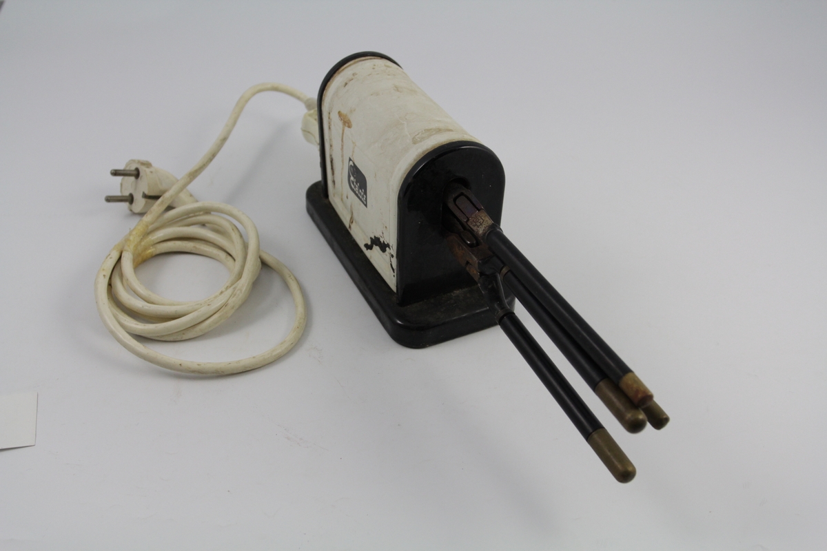 Eletrisk krølltang bestående av fire deler:
a-b) krølltenger: 2 stk. sylindriske håndtak (a kan beveges).  Når håndtakene føres sammen, presses sylinder i andre enden ned i hul del. 
c) elektrisk varmeapparat, uttak støpsel og ledning på den ene siden. Rektangulær sokkel. Påsatt rektangulær del med avrundet overside. Kortside: inntak for to krølltenger. Oval åpning. 
d) Ledning med kontakter.