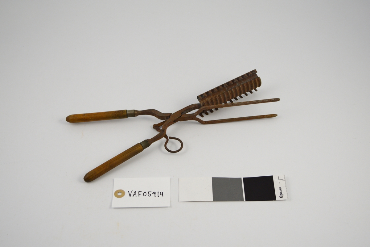 Krølltang: To jern som krysser hverandre i et hengslingsparti, og hvor den ene stang er stukket gjennom den andre. Sammenhengslingen er klinket. Det ene "jern" har to runde tynne tinder stående i spiss u-form og med butte ender. Det andre "jern" består av to deler, en fast og en bevegelig. Den flat utformede og avkuttede "arm" er festet med to nagler til et krumbøyd stykke lettmetall med 12 rett oppstående tagger på hver side. På oversiden av det krumbøyde lettmetall er lagt et 3 cm bredt rektangulært stykke lettmetall med tversgående rifler. Det riflete lettmetallstykket er bevegelig innenfor et rektangulært felt (hull), på undersiden av det andre lettmetallstykket, og hvor det er naglet fast til en bevegelig "arm". Denne "arm" består av to sammen-naglete deler stående vinkelrett på hverandre, den korte del avsluttes med en bøyd krok for fingergrep. Håndtakene dreiet med avrundet spiss i den ene enden, to metallringer markerer overgangen til jernene.