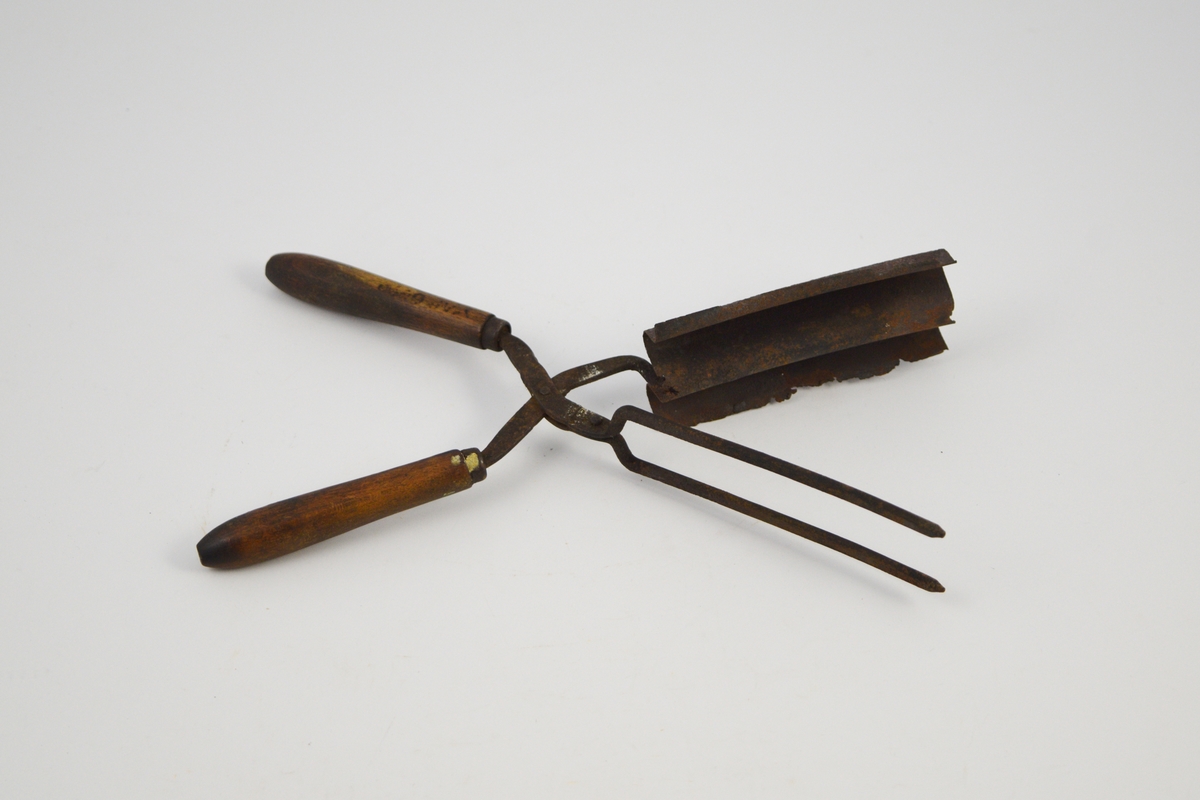 Krølltang med to håndtak i tre og to sylinderformede tinner, festet til en bølgeformet blikkplate som er tilpasset den andre armens tinner.