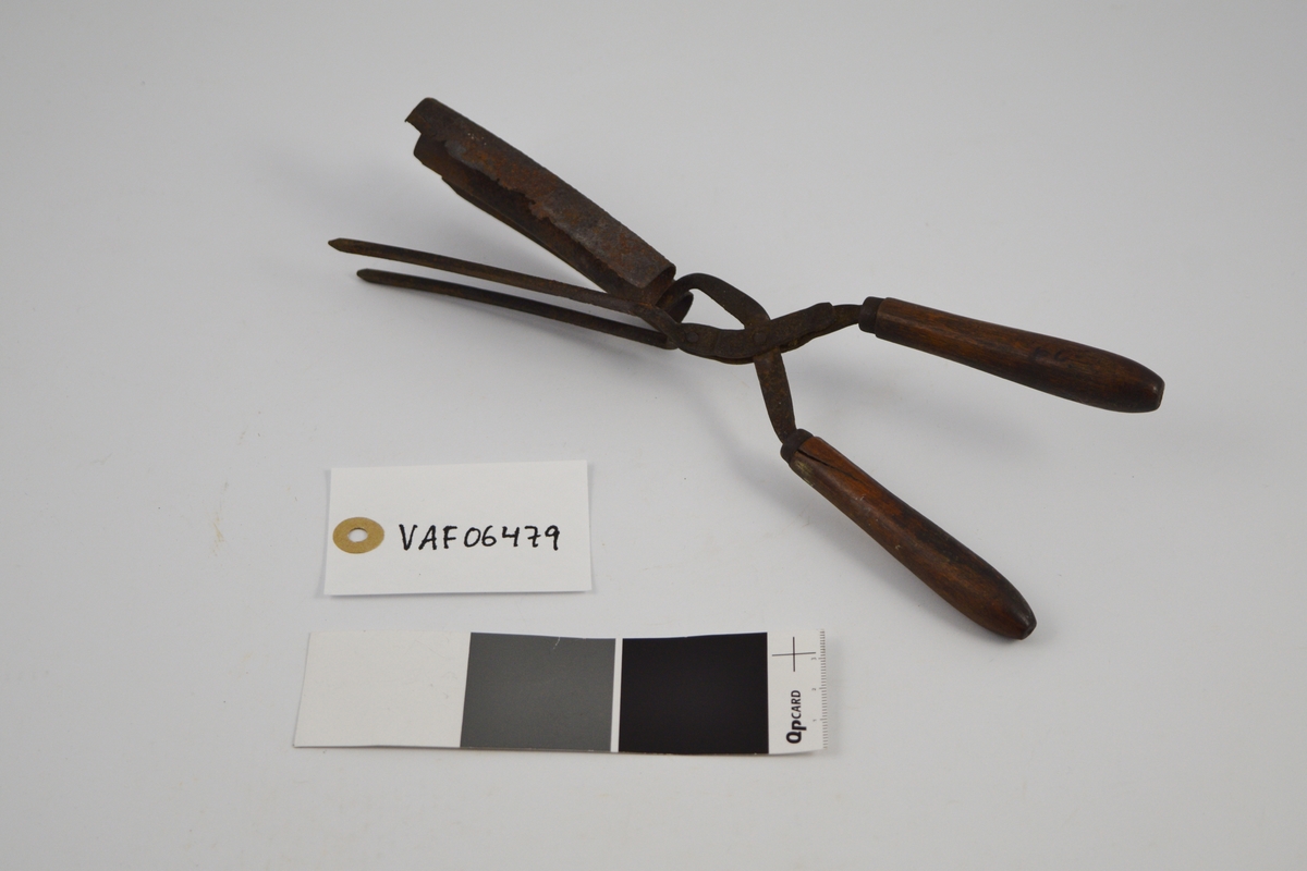 Krølltang med to håndtak i tre og to sylinderformede tinner, festet til en bølgeformet blikkplate som er tilpasset den andre armens tinner.