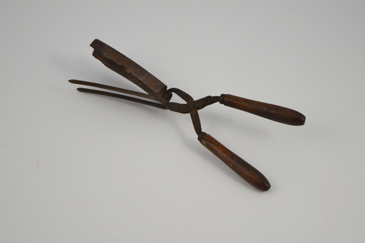 Krølltang med to håndtak i tre og to sylinderformede tinner, festet til en bølgeformet blikkplate som er tilpasset den andre armens tinner.