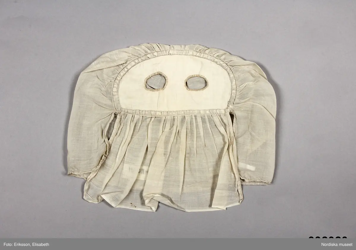 Tunn beige ansiktsmask av textil. Utformad som en huva med två hål för ögonen. Anm: Masken har några små fläckar. Märt med en textillapp med Kriminalvårdsstyrelsens nummer N-110091.
/Johanna Skoglund 2013-04-22
