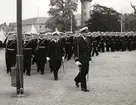 Flottans militärer med sjöbefäl marcherar runt på stortorget. I bakgrunden syns vattentornet.