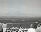Ett publikhav blickar ner mot havet där ett antal örlogsfartyg syns på linje efter varandra. Bilden är tagen i samband med 