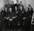 Konteramiral Johan Erik Samuelson poserar för ett gruppfoto tillsammans med en kommendörkapten och flera kaptener och högre militära tjänstemän. Bland dem finns även kommendörkapten av första graden Bengt Lind af Hageby (andra från vänster, nedersta raden).