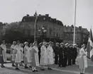 Uniformsklädda militärer och dräktklädda kvinnor står uppställda på Stortorget i Karlskrona. Längst fram står en kvinna med en svensk flagga.