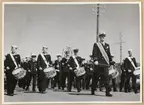 Marinens musikkår på marsch. Främst syns dirigenten, bakom honom första raden trumslagare.