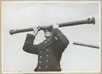 En uniformsklädd man håller upp ett kikarsikte till ögonen som ser åt två olika håll.