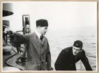Två uniformsklädda militärer ombord på ett fartyg. Den ena mannen höjer handen och pekar med ett finger.