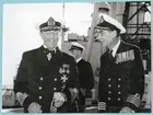 Konteramiral Samuelson och chefen för H.M.S. Montclare, Captain Hutchinson, i glatt samspråk. De står ombord på H.M.S. Montclare. Båda är klädda i uniform med medaljer på bröstet samt i mössa. I bakgrunden syns ytterligare en militär. Från Engelska besöket i Karlskrona den 9-14 september 1951.