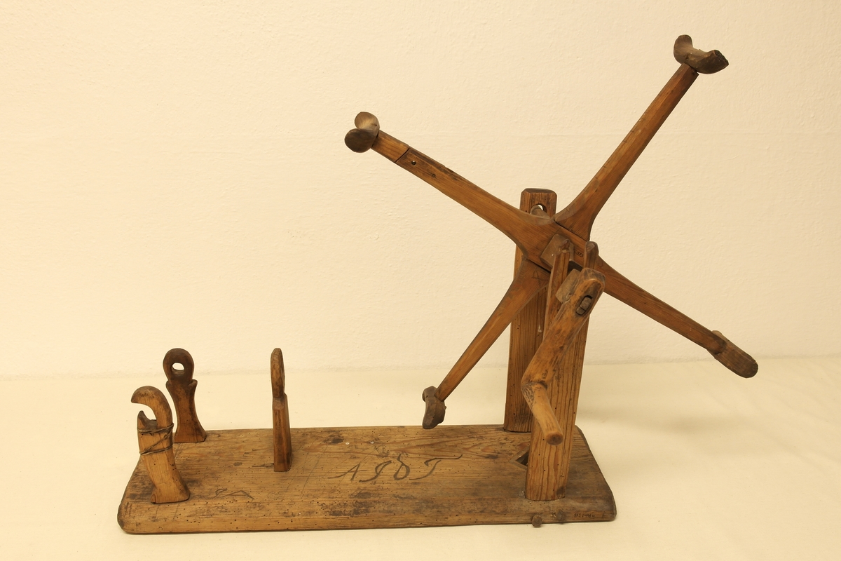 Garnvinde i tre. Stativ festet på ei plate (a). På stativet er det to pinner i kryss (b) som er roterbart ved hjelp av ei sveiv. Det er inngravert initialer og tall i plata, både på oversiden og undersiden.