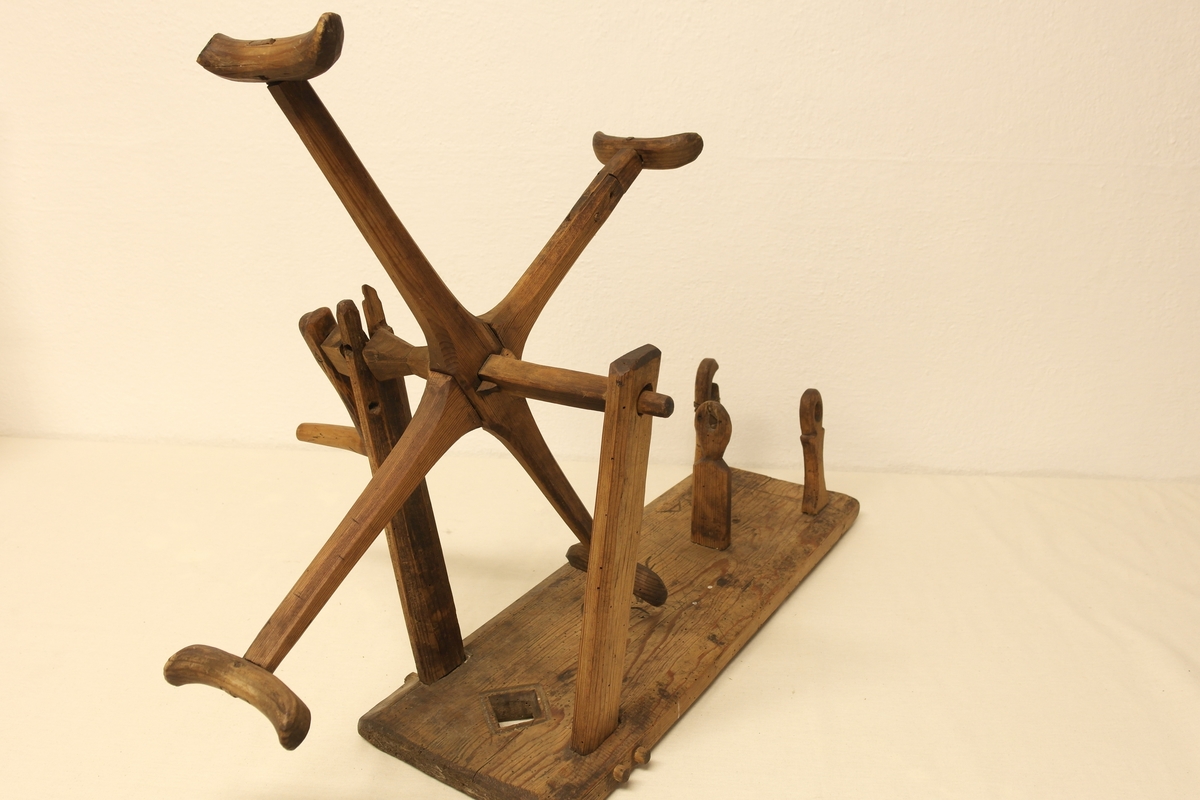 Garnvinde i tre. Stativ festet på ei plate (a). På stativet er det to pinner i kryss (b) som er roterbart ved hjelp av ei sveiv. Det er inngravert initialer og tall i plata, både på oversiden og undersiden.