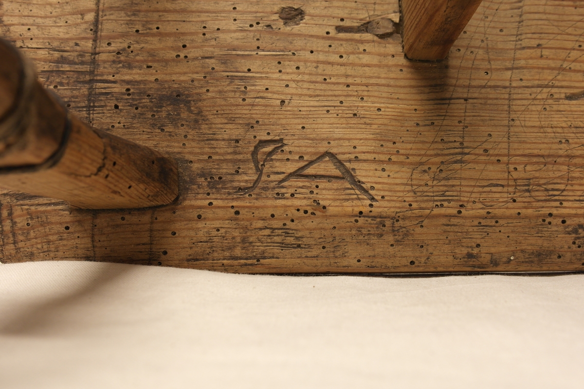 Garnvinde i tre. Stativ festet på ei plate (a). På stativet er det to pinner i kryss (b) som er roterbart ved hjelp av ei sveiv. Det er inngravert initialer og tall i plata, både på oversiden og undersiden.