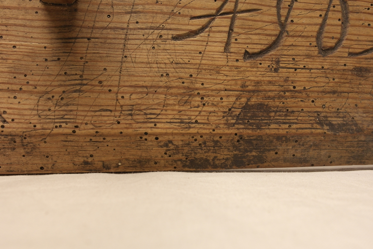 Garnvinde i tre. Stativ festet på ei plate (a). På stativet er det to pinner i kryss (b) som er roterbart ved hjelp av ei sveiv. Det er inngravert initialer og tall i plata, både på oversiden og undersiden.