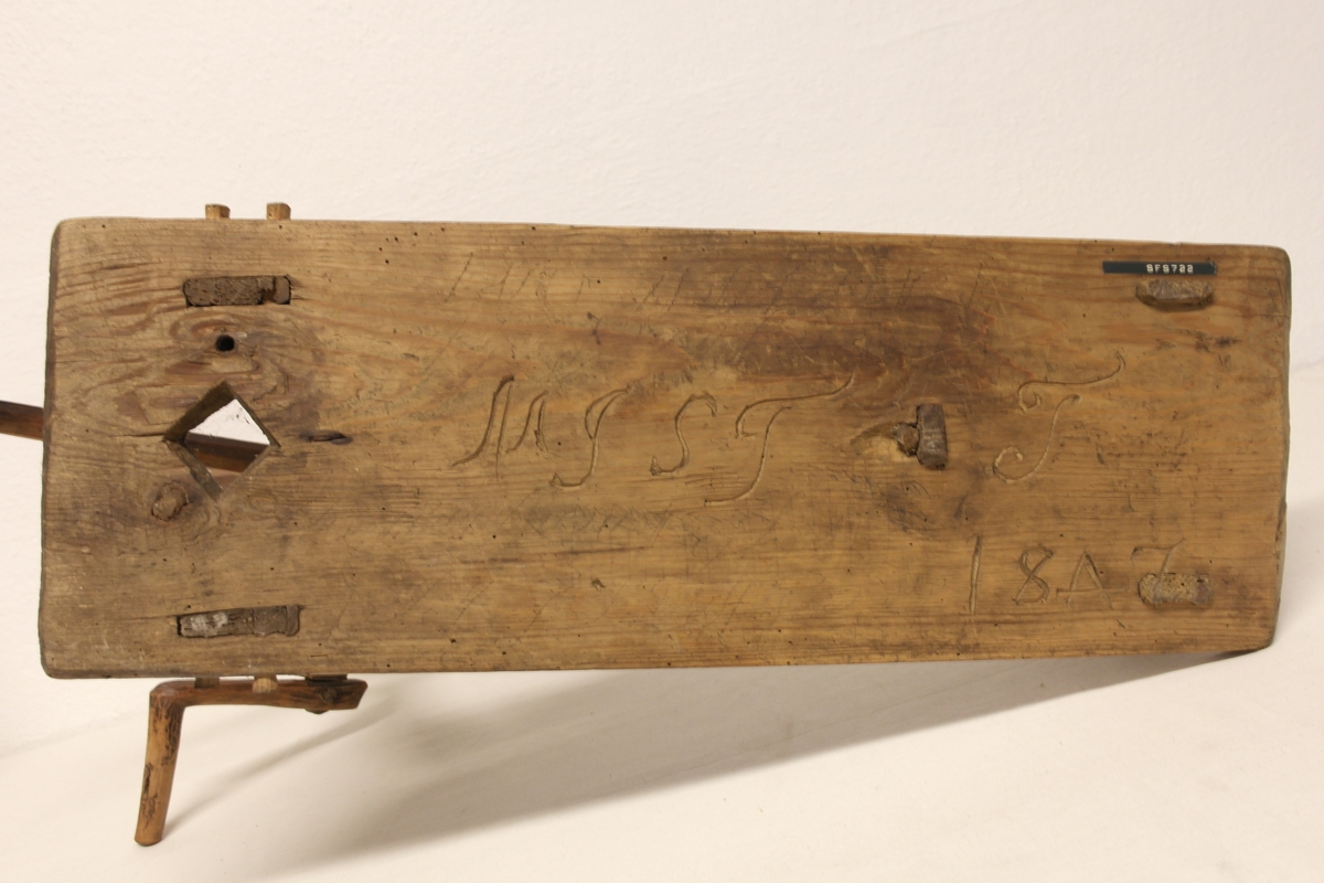 Garnvinde i tre. Stativ festet på ei plate (a). På stativet er det to pinner i kryss (b) som er roterbart ved hjelp av ei sveiv. Det er inngravert initialer og tall i plata, både på oversiden og undersiden.