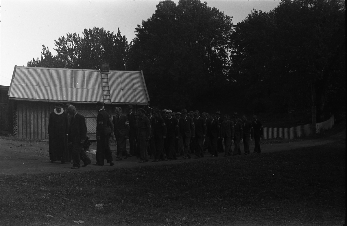 Fem bilder fra en høytidelighet på Hoff kirkegård, sannsynligvis 16. september 1945 som var en minnedag for de som falt under 2.verdenskrig.. Markering foregår sannsynligvis ved graven til Bjarne Fodstad som falt ved Haug kirke i Vardal 21.april 1940. Prosesjonen utgjøres av, foruten sogneprest Ingebrigt Hole, medlemmer av Milorg-gruppa Kapp/Lena. På bilde nr. 1 er også følgende personer identifisert: Johan Nygaard i venstre bildekant, Carsten Aschim bakerst i rekka nærmest Nygaard, og trolig Harald Tørnby som nr. 2 i rekke nr. 2.