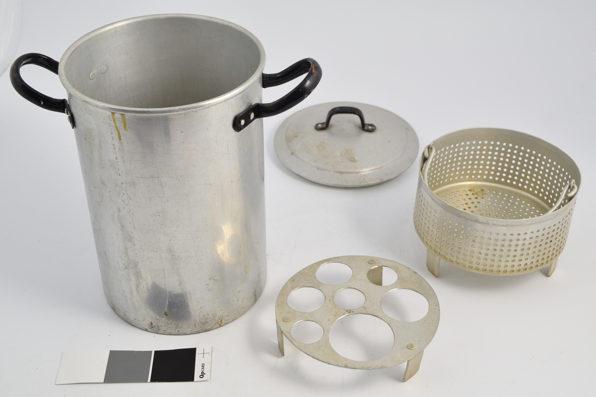 Aluminiumskjele med lokk og ot haker. To aluminiums innsatser; en med små hull og en med store hull - begge på ben. Brukt til varmebehandling (desinfisering) av kolber og utstyr og enkelte legemidler. Vann ble fylt opp til bunnen av risten og varmet opp.