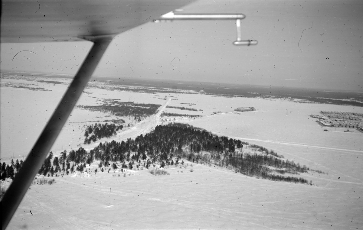 Flygfotografi av skogsparti och Veitsiluoto samhälle (i högerkant). Bild från F 19, Svenska frivilligkåren i Finland. Med flygplansvinge i förgrunden.