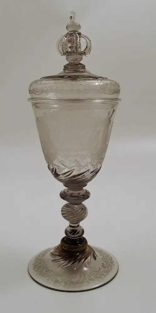 Pokal med lokk med konisk klokke. Gravert dekor og innskrifter. Treleddet stett med utvendige spiraler og luftbobler. Hvelvet fotplate med gravert ranke. Hvelvet lokk med krone, kule og kors samt løv, gravert rokokkoranke og innskrift. Løv på klokkens nederste del og på fotplate. Fotplaten er festet til stetten med en metallring