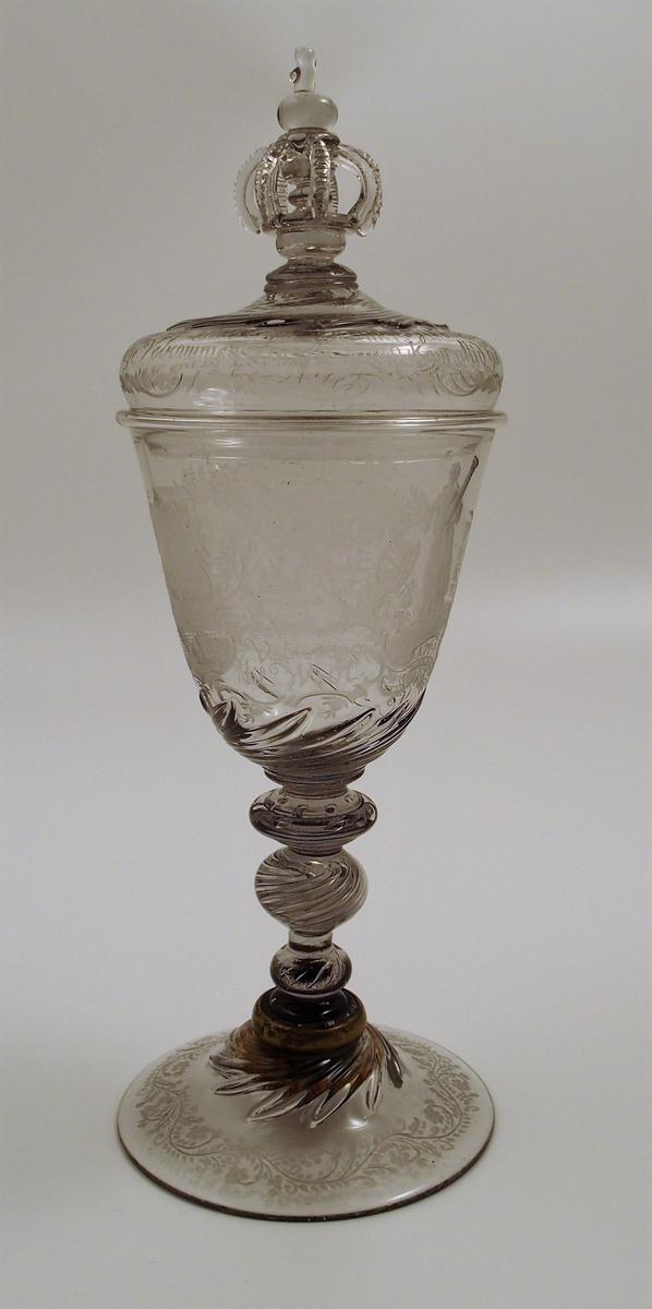 Pokal med lokk med konisk klokke. Gravert dekor og innskrifter. Treleddet stett med utvendige spiraler og luftbobler. Hvelvet fotplate med gravert ranke. Hvelvet lokk med krone, kule og kors samt løv, gravert rokokkoranke og innskrift. Løv på klokkens nederste del og på fotplate. Fotplaten er festet til stetten med en metallring