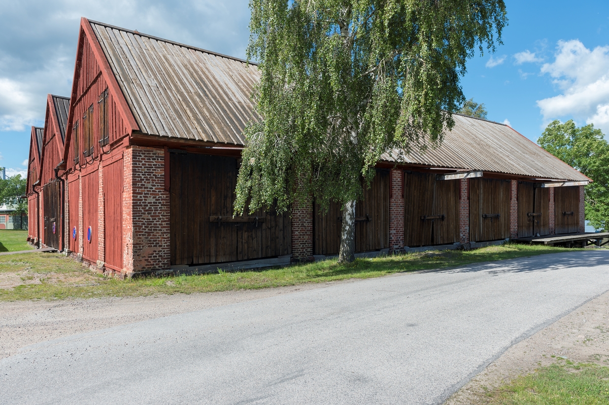 Rött ekvirkesskjul i en våning med vind. Byggnaden är sammansatt av tre "skepp" med brädklädda sadeltak.