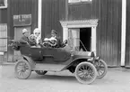 Handlare Georg Elmberg med hustrun Anna Ottilia med barn framför parets handelsbod Solhaga i Österbymo. Barnen kan antas vara makarnas tre förstfödda överlevande, Margit Maria Margareta (f. 1908), Brita Ingegärd Margareta (f. 1909) och Clarence Birger Georg (f. 1911). Chaffören antas vara Bror Konstans Salomon Sahlström, boende i Lilla Mohaga. Bilen är förövrigt en T-Ford från cirka 1911 med modifierad touring-kaross.