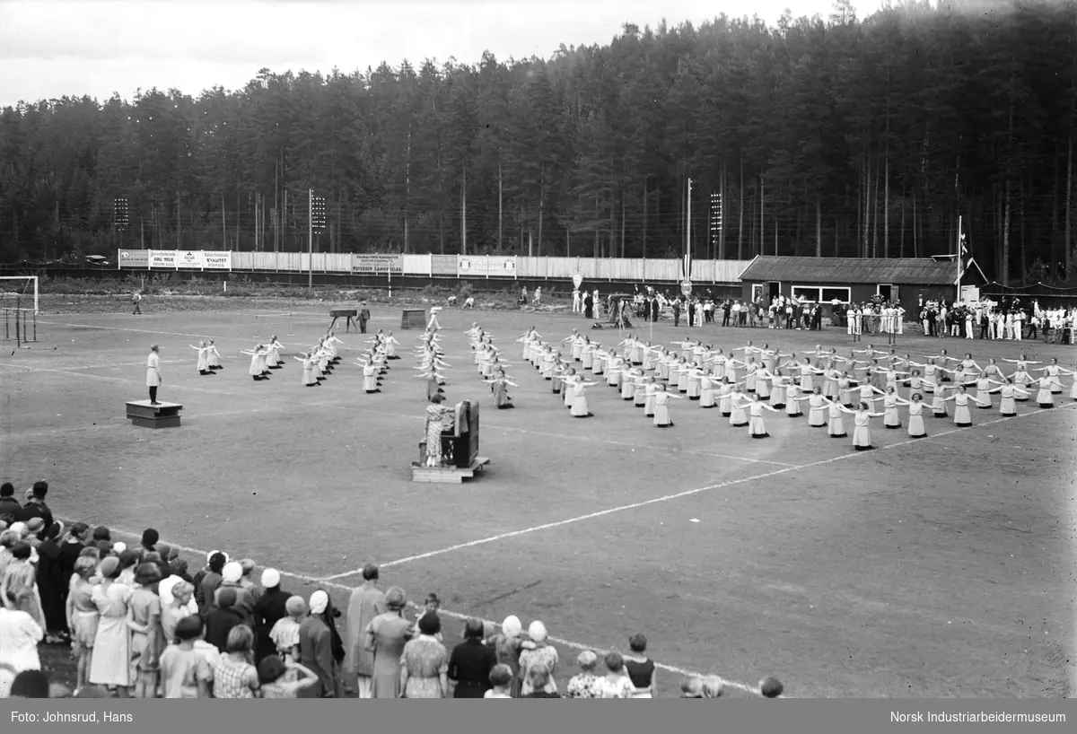 Turnstevne 1933. Turndamer har oppvisning, to kvinner ved piano på gresset. Tilskuere rundt stadion.