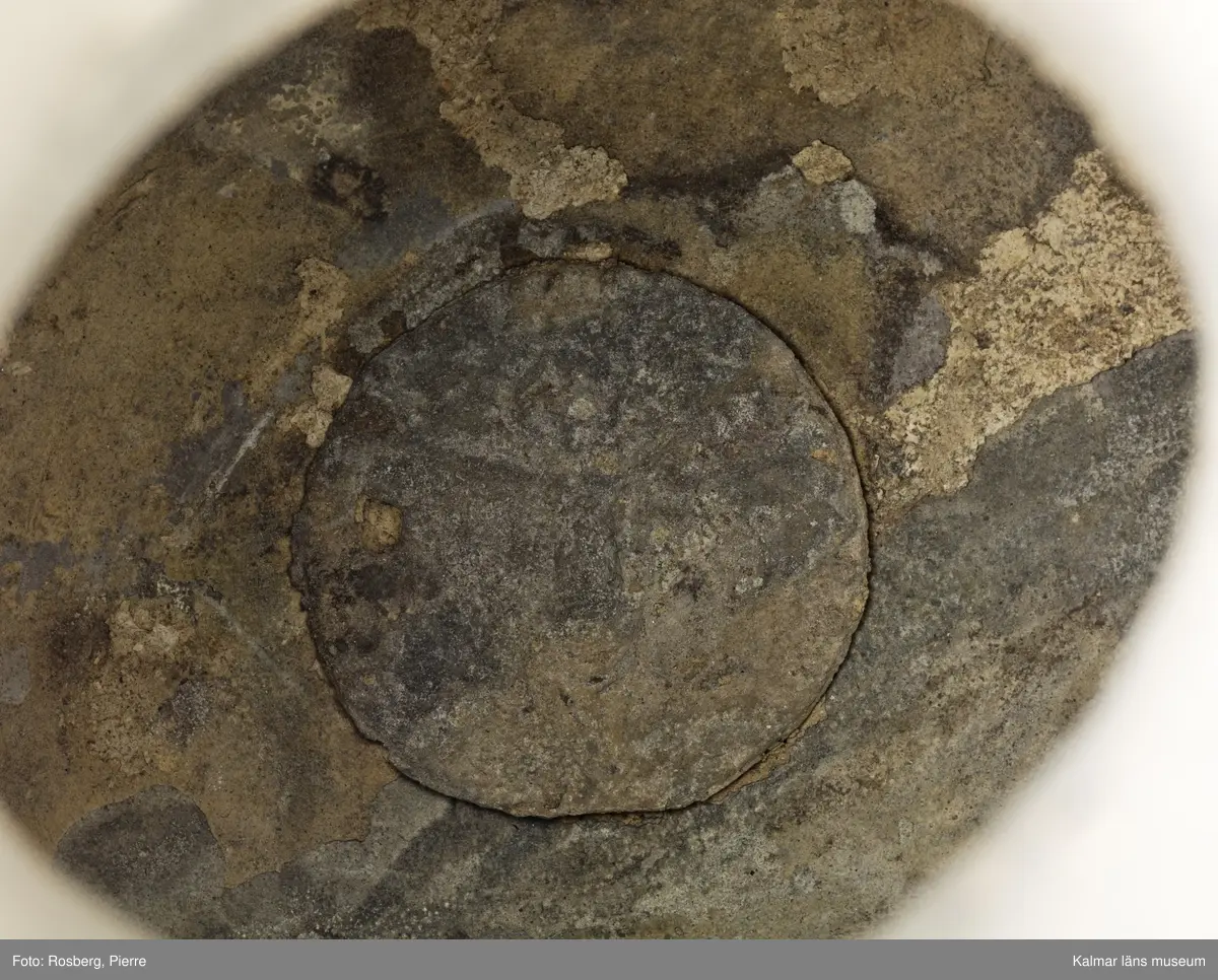 KLM 1886. Kanna, hankkärl. Av tenn. Hankkärl, bukig form, försedd med lock och handtag men utan näbb. Grepen ornerad på utsidan med bladranka som upptill avslutas med en djurliknande figur. Bottenmedalj i kannan, i form av korsfästelsemedalj. Spår efter förlorad lockmedalj, på lockets insida.