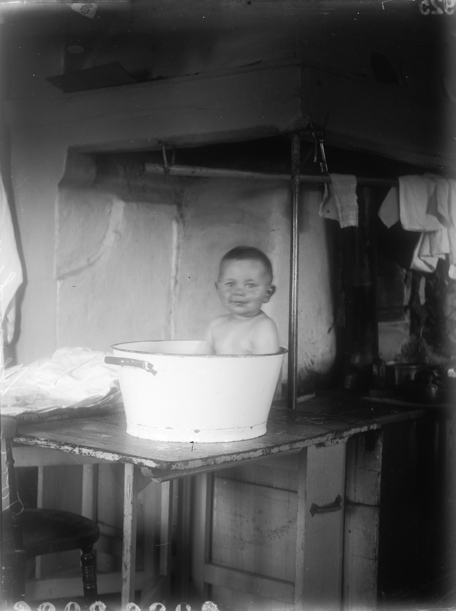 Tore Alinder badar i balja på bord i köket, Sävasta, Altuna socken, Uppland 1925