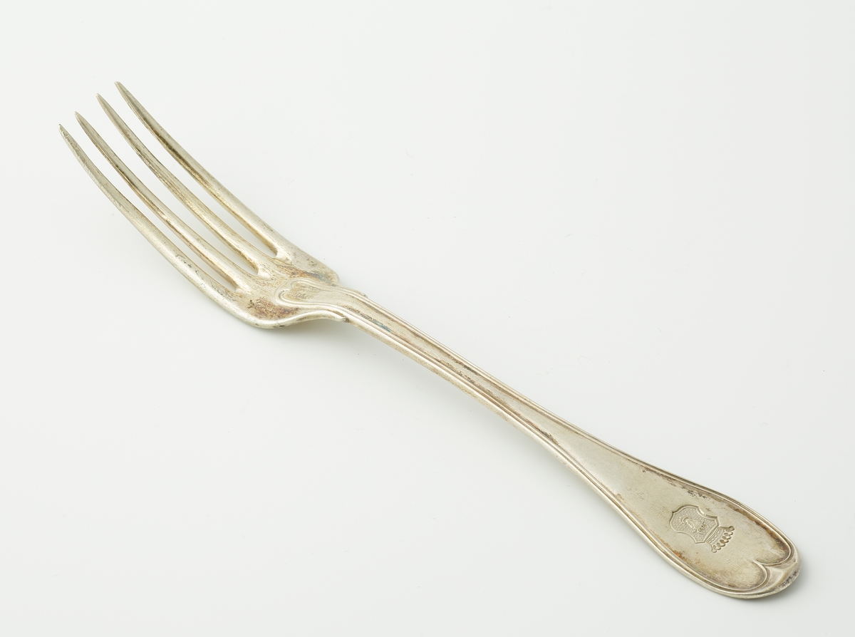 Matgaffel i silver.
Svensk trubbig modell. Präglat adelsvapen (friherrekrona med hjärtvapen i form av oxhuvud)* på skaftet.

*Friherrliga ätten von Mecklenburg (ointroducerad tysk/svensk adel).