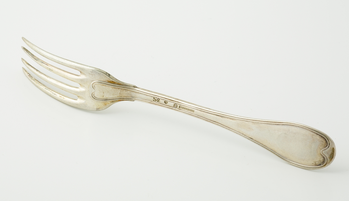 Matgaffel i silver.
Svensk trubbig modell. Präglat adelsvapen (friherrekrona med hjärtvapen i form av oxhuvud)* på skaftet.

*Friherrliga ätten von Mecklenburg (ointroducerad tysk/svensk adel).