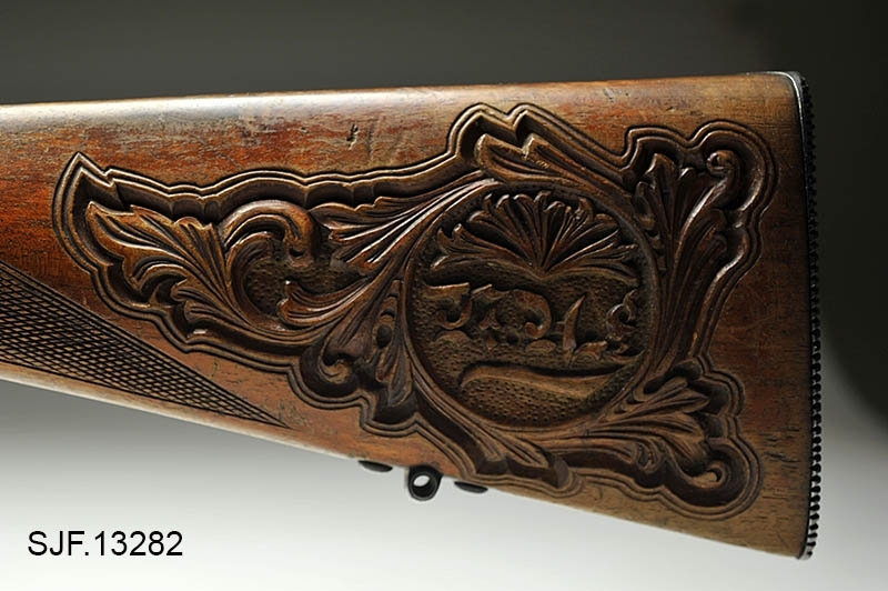 Krag-Jørgensen rifle med kaliber 6, 5 x 55. Geværet har pistolgrep. Magasinkapasitet på 5 patroner. Kolben er brunbeiset / oljet. Skjeftet er dekorert med forseggjorte utskjæringer.  Kolbekappen av stål har innfelt et lokk. Om man åpner lokkket kommer man til et "oppbevaringsrom" i kolben. Treverket som omslutter undersiden av geværløpet har noen sprekkdannelser.  Geværet er utstyrt med høydejusterbart skur og sidejusterbart korn. 