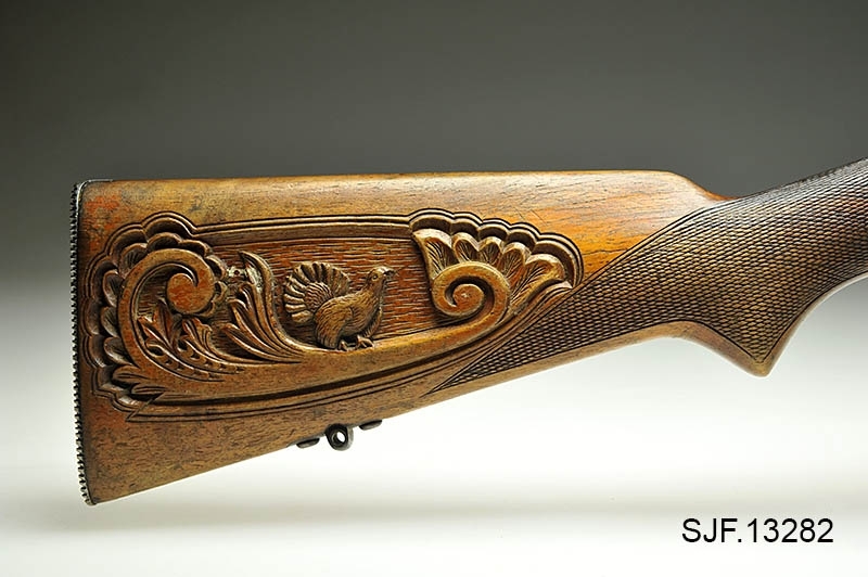 Krag-Jørgensen rifle med kaliber 6, 5 x 55. Geværet har pistolgrep. Magasinkapasitet på 5 patroner. Kolben er brunbeiset / oljet. Skjeftet er dekorert med forseggjorte utskjæringer.  Kolbekappen av stål har innfelt et lokk. Om man åpner lokkket kommer man til et "oppbevaringsrom" i kolben. Treverket som omslutter undersiden av geværløpet har noen sprekkdannelser.  Geværet er utstyrt med høydejusterbart skur og sidejusterbart korn. 