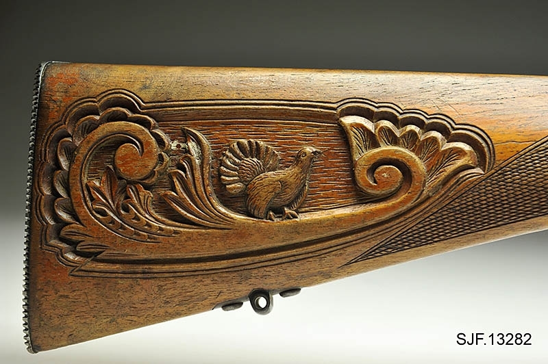 Krag-Jørgensen rifle med kaliber 6, 5 x 55. Geværet har pistolgrep. Magasinkapasitet på 5 patroner. Kolben er brunbeiset / oljet. Skjeftet er dekorert med forseggjorte utskjæringer.  Kolbekappen av stål har innfelt et lokk. Om man åpner lokkket kommer man til et "oppbevaringsrom" i kolben. Treverket som omslutter undersiden av geværløpet har noen sprekkdannelser.  Geværet er utstyrt med høydejusterbart skur og sidejusterbart korn. 