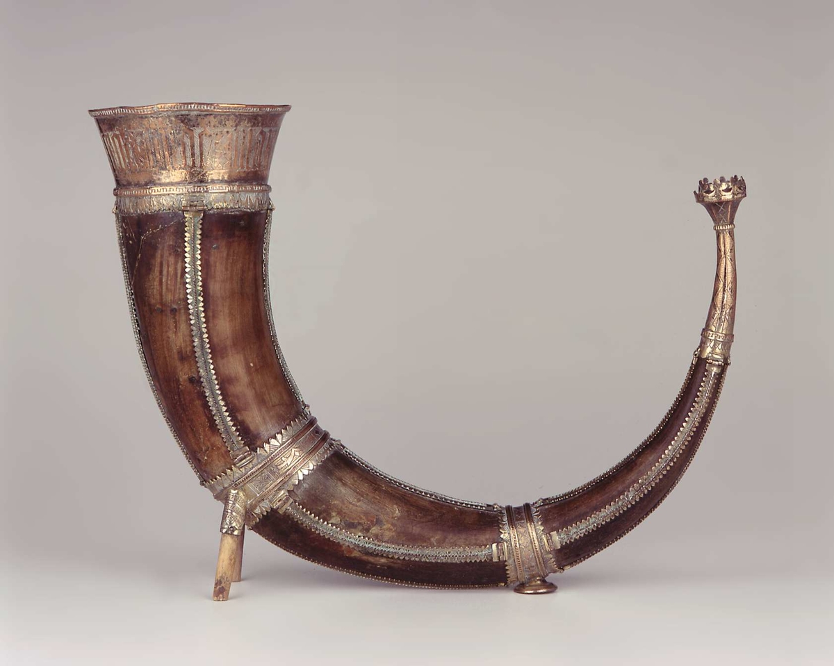 Drikkehorn med metallbeslag rundt kanten, to ringer rundt hornet, et beslag på spissen og smale langsgående beslag. Den største ringen har fester for støttebein. De nåværende beina er ikke de opprinnelige. Beslagene er av forgylt bronse. Krone i spissen. Graverte beslag med geometriske border.