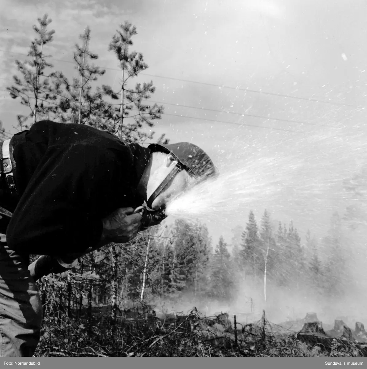 Hyggesbränning. Människor med risruskor jobbar med att begränsa elden. En brandman dricker ur vattenslangen.  Okänd ort.