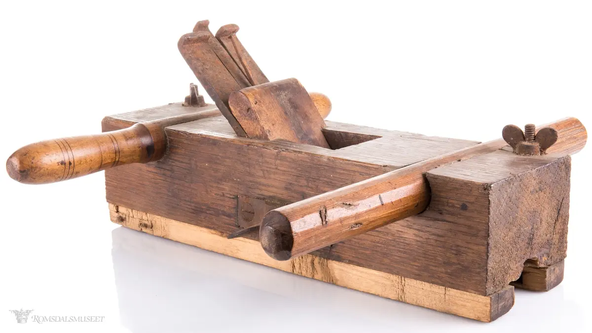 Rektangulær okshøvel med jern og kile. Jernet kan reguleres med skrumekanisme. Et dreid og et skåret håndtak er felt ned i avrundede spor foran og bak. Spor for høvling av fjær i sålen og regulerbare styringslister på hver side av sporet.