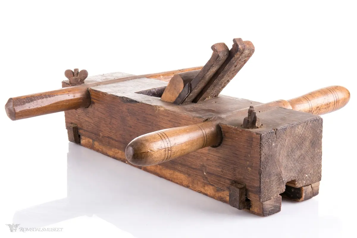 Rektangulær okshøvel med jern og kile. Jernet kan reguleres med skrumekanisme. Et dreid og et skåret håndtak er felt ned i avrundede spor foran og bak. Spor for høvling av fjær i sålen og regulerbare styringslister på hver side av sporet.