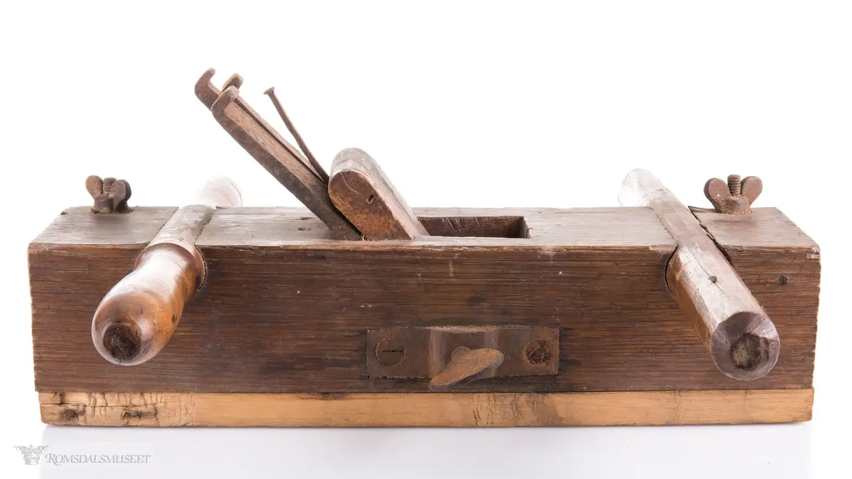 Rektangulær okshøvel med jern og kile. Jernet kan reguleres med skrumekanisme. Et dreid og et skåret håndtak er felt ned i avrundede spor foran og bak. Spor for høvling av fjær i sålen og regulerbare styringslister på hver side av sporet.