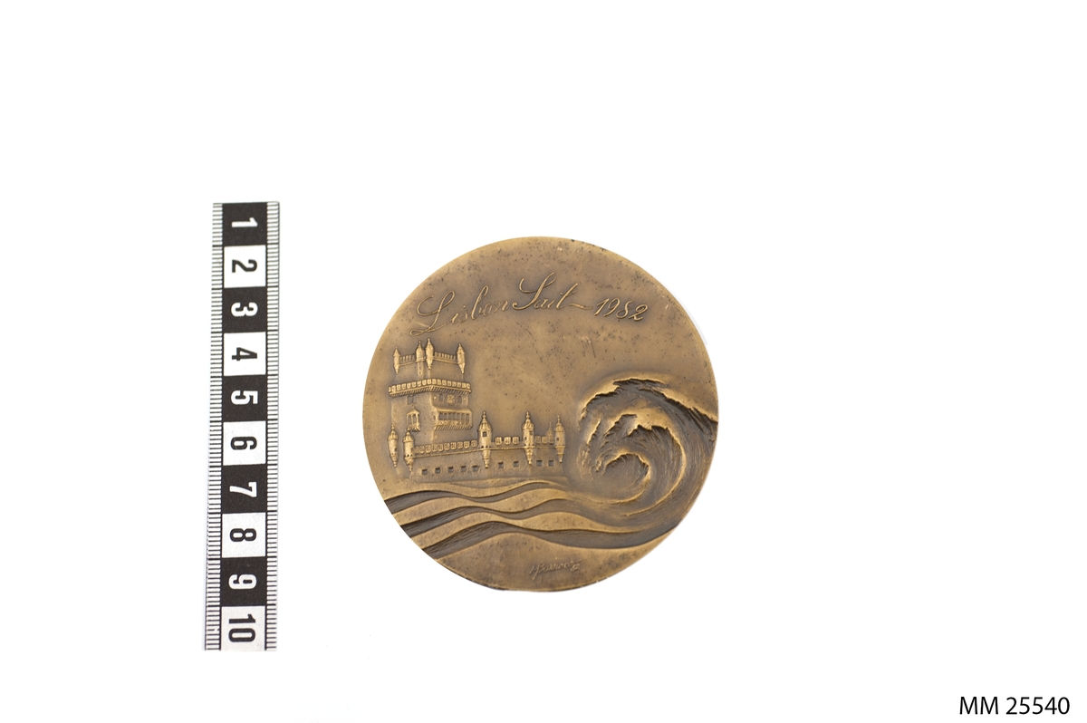 Rund plakett i metall med texten "Lisbon Sail - 1982" ovanför en relief av en borg och en stor rullande våg. Tillverkarsignaturen M. Barroco 82 står i nederkanten av denna våg. På andra sidan finns texten "APORVELA" och "ASSOCIACÂO PORTUGUESA DE TREINO DE VELA" runt en bild av segel med kors på.