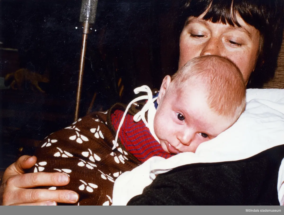 Lilla Karin (född 17 februari 1978) vilar tryggt på sin mor Ingers vänstra axel. Den bruna sparkdräkten finns i Mölndals stadsmuseums samlingar med invnr. 05203.