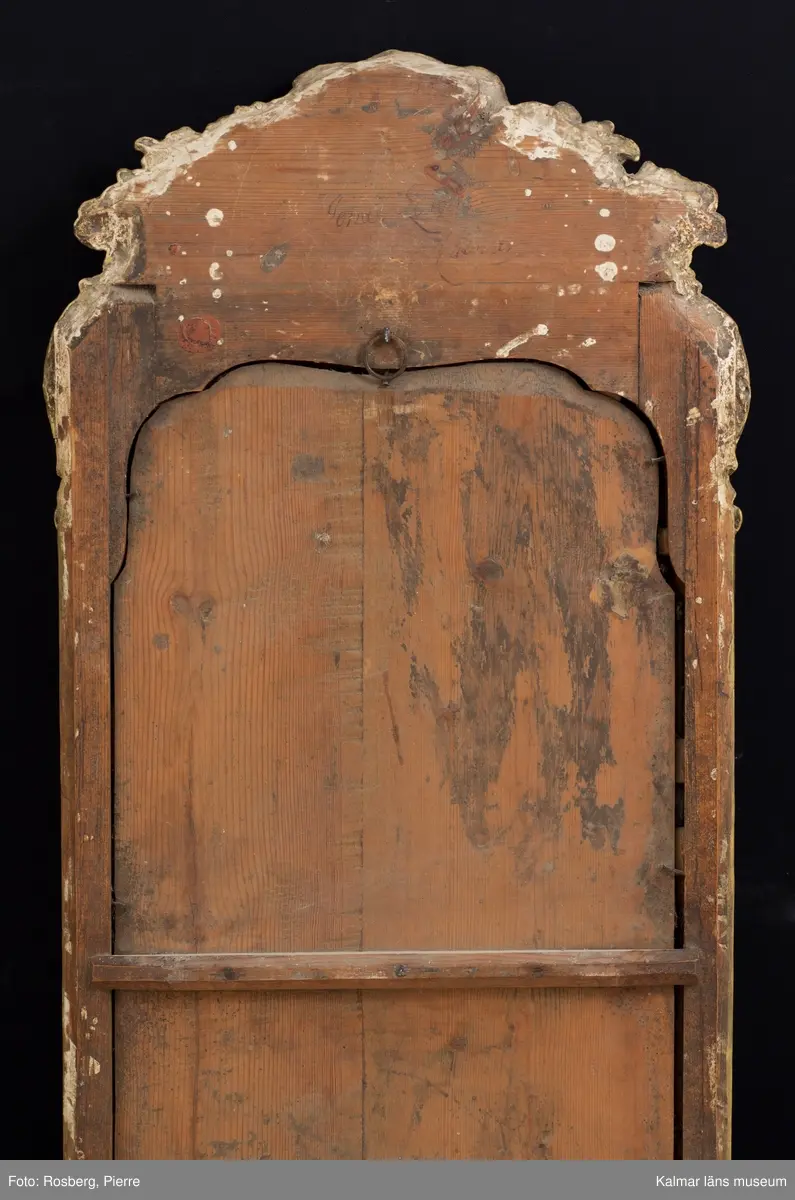 KLM 14346. Spegel, väggspegel. Förgylld ram av trä med snidade rokokoornament. Spegelglaset i två delar, facetterat, det övre spräckt. På baksidan Kalmar hallstämpel (ej den vanliga) samt otydlig signatur, troligen: Jonas Löw Kalmar. Rokoko.