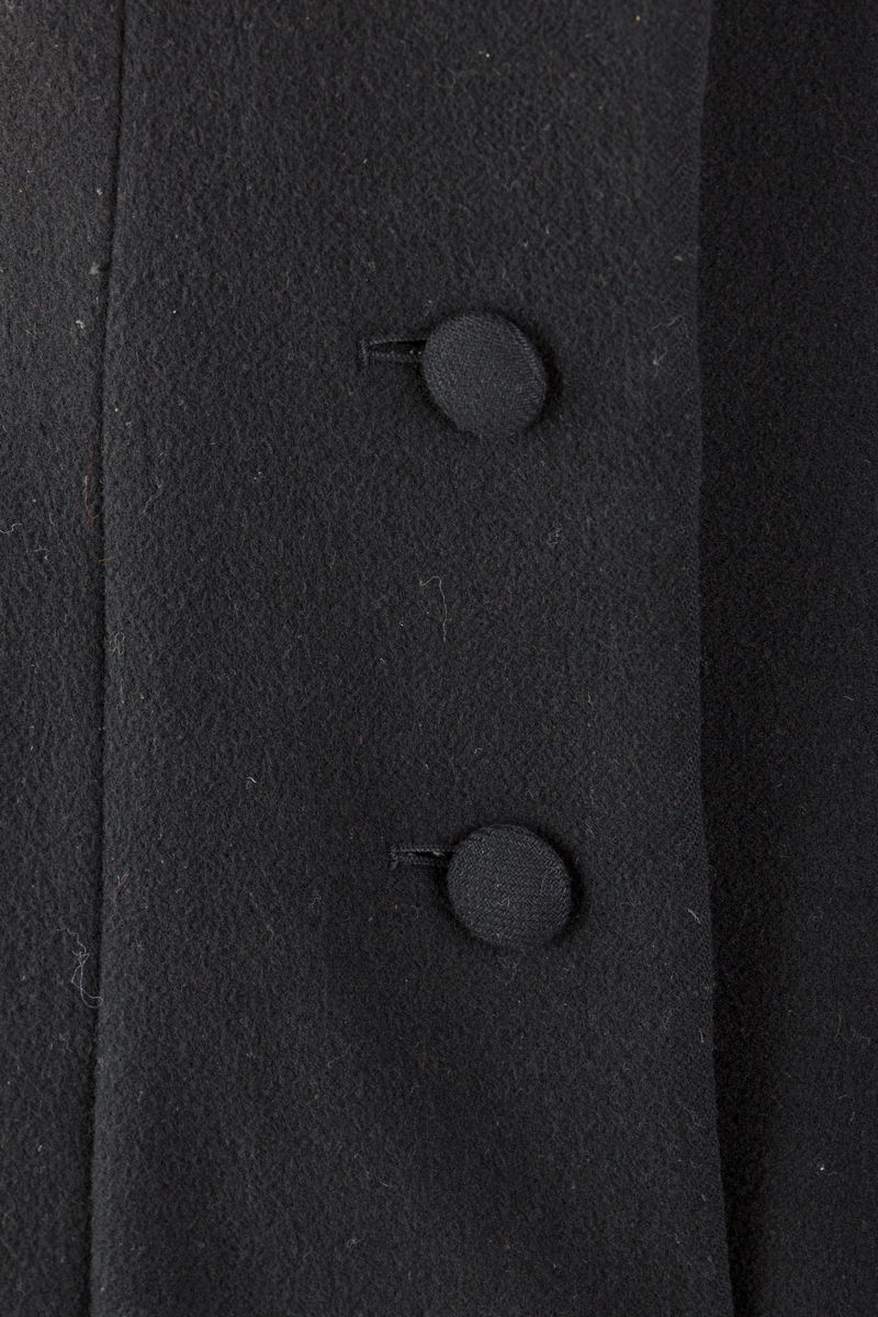 Innsvinget liv, pynteklaffer ved brystet foran. 
Stikklommer foran.
Skulderputer
Fire trukne knapper
Avrundet krage