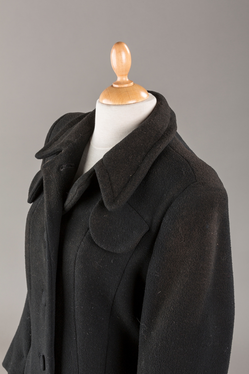 Innsvinget liv, pynteklaffer ved brystet foran. 
Stikklommer foran.
Skulderputer
Fire trukne knapper
Avrundet krage